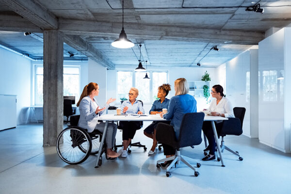 Image is stock photo of 5 people sat facing each other around a work table.
